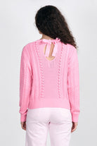 Brown haired female model wearing Jumper1234 Pink cotton aran crew neck jumper with a ribbon tie back facing away from the camera