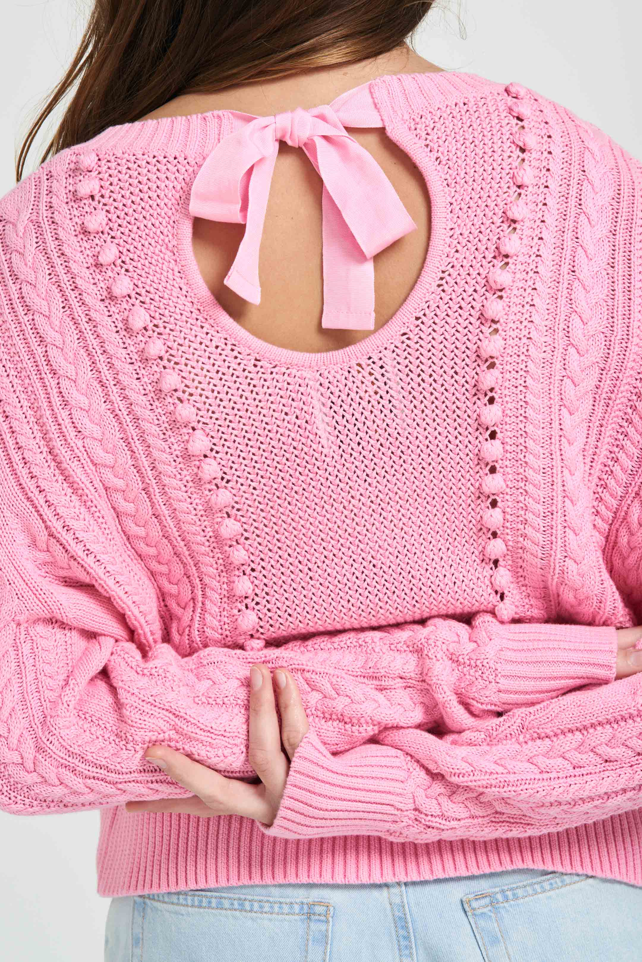 Brown haired female model wearing Jumper1234 Pink cotton aran crew neck jumper with a ribbon tie back close up