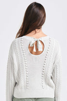 Brown haired female model wearing Jumper1234 Silver marl cotton aran crew neck jumper with a ribbon tie back facing away from the camera