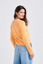 Brown haired female model wearing Jumper1234 Apricot cotton crew neck jumper with a diamond texture stitch pattern facing away from the camera