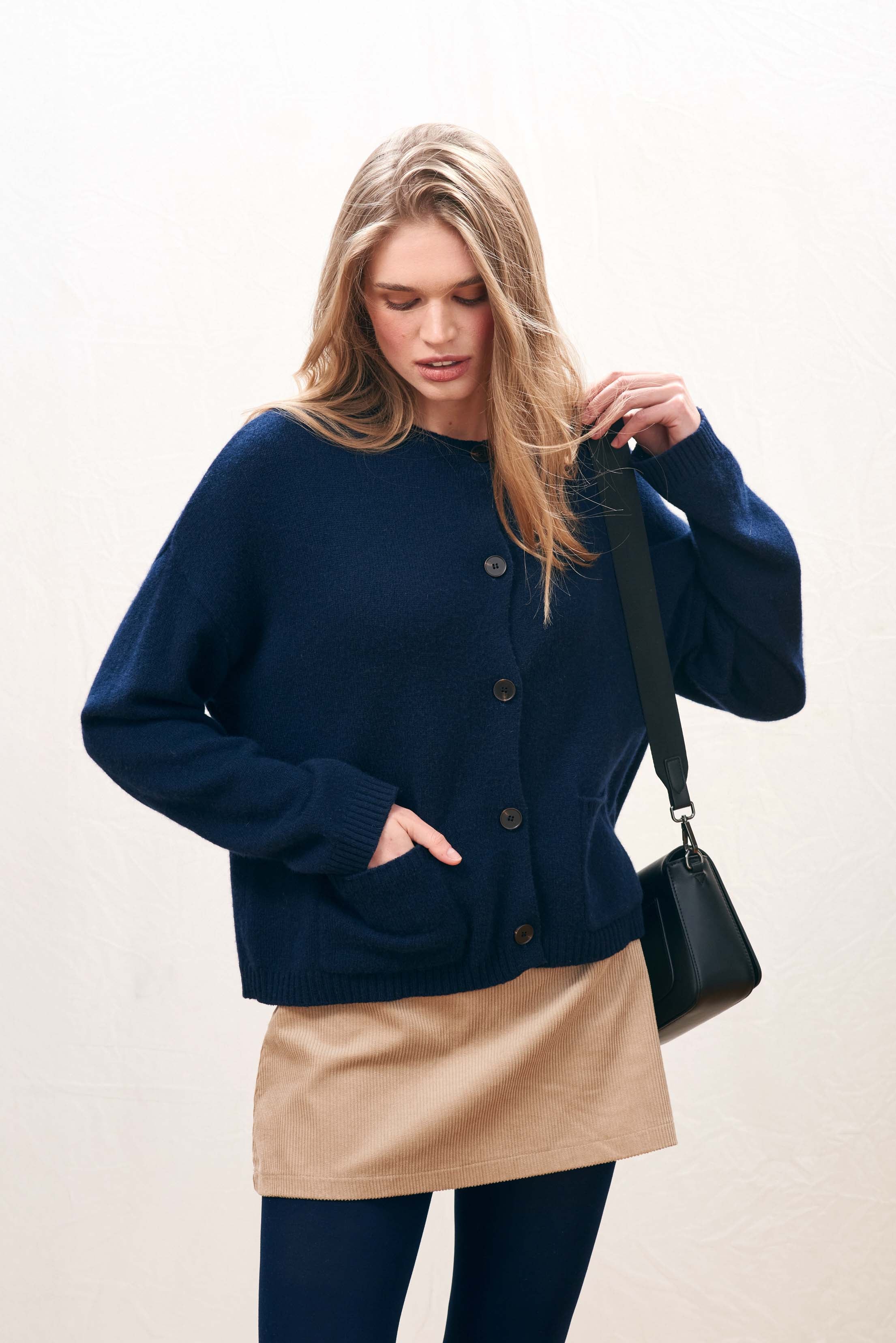 Female model wearing Jumper 1234 Heavier weight cashmere crew neck cardigan in navy. Oversize fit, two pockets and a fabulous cable detail at the back neck.