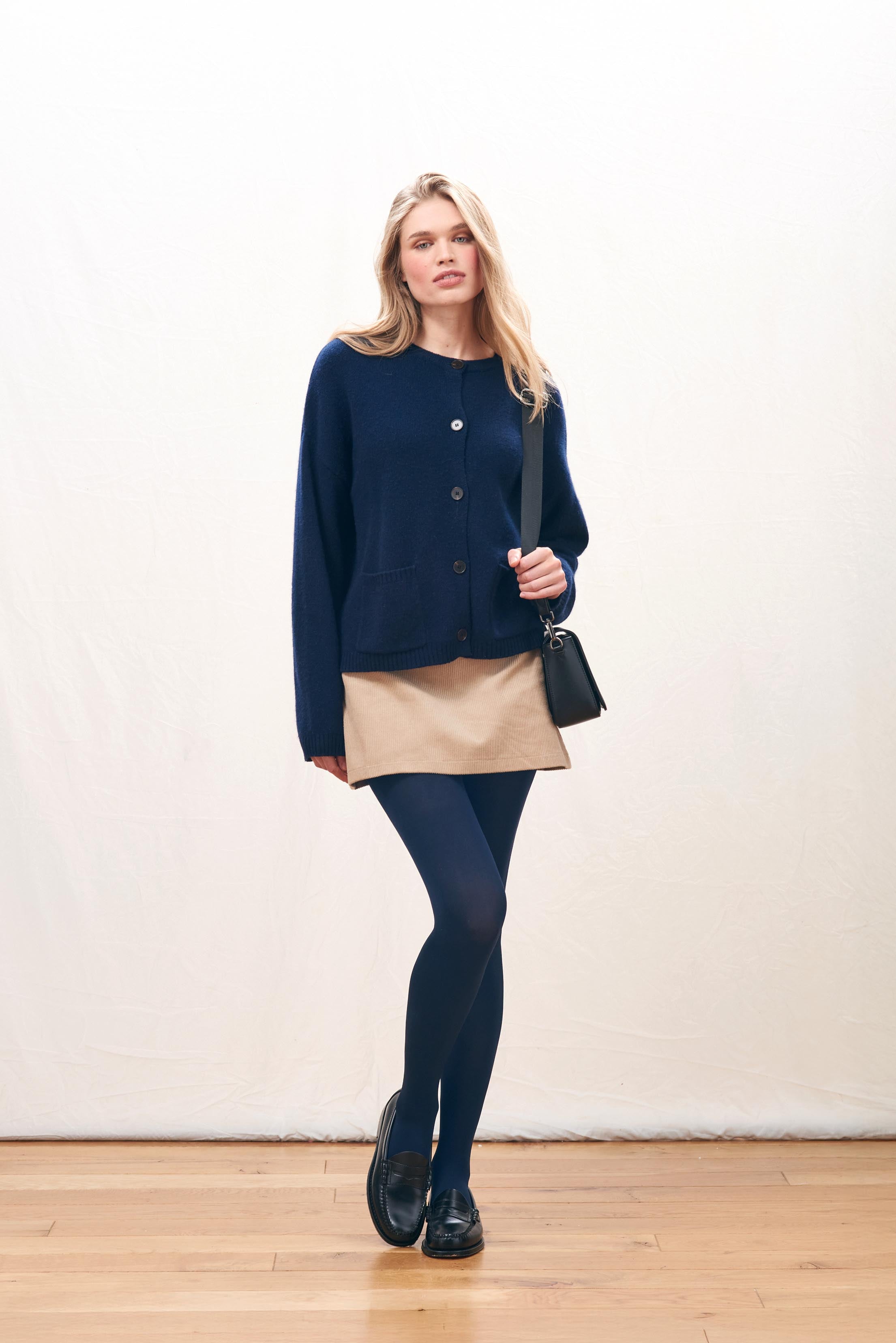 Female model wearing Jumper 1234 Heavier weight cashmere crew neck cardigan in navy. Oversize fit, two pockets and a fabulous cable detail at the back neck.
