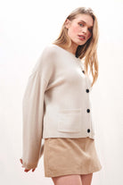 Female model wearing Jumper 1234 Heavier weight cashmere crew neck cardigan in stone. Oversize fit, two pockets and a fabulous cable detail at the back neck.
