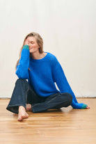 Female model sat wearing Jumper 1234 hand knitted mohair and wool blend hand knitted crew neck jumper in blue with green tipping.