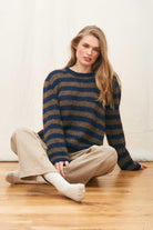 Female model sat on the floor wearing Jumper 1234 hand knitted mohair and wool blend hand knitted crew neck jumper in navy and chocolate stripes.