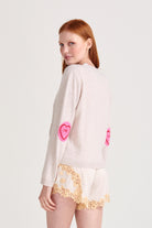 Red haired model wearing Jumper1234 Oatmeal cashmere vee neck cardigan with pink and red love hearts intarsia elbow patches facing away from the camera