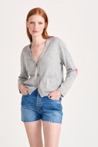 Red haired model wearing Jumper1234 Grey cashmere vee neck cardigan with pink and red love hearts intarsia elbow patches facing away from the camera