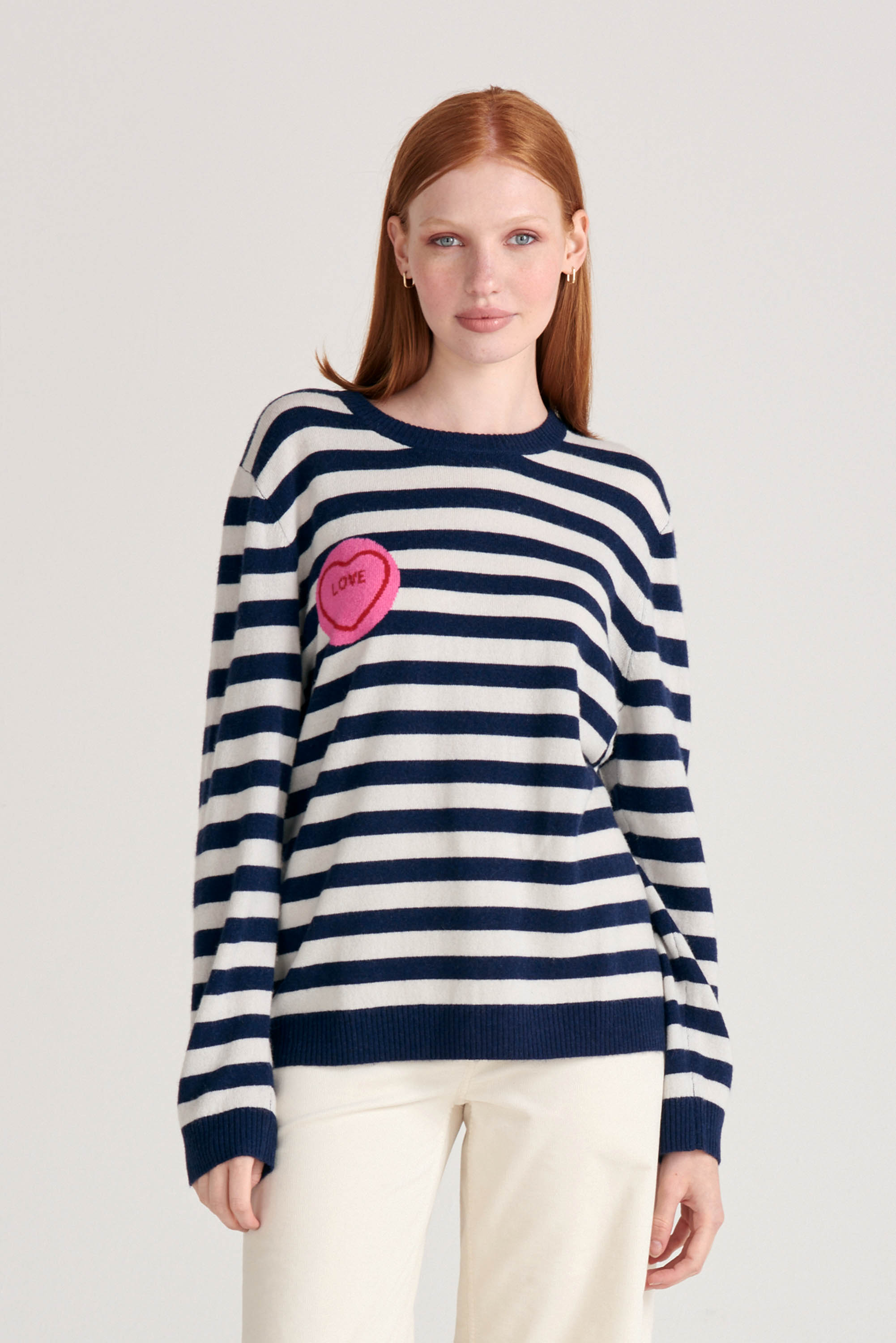 Red haired female model wearing Jumper1234 Navy and cream stripe cashmere and wool mix crew neck jumper with pink and red love heart intarsia