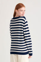 Red haired female model wearing Jumper1234 Navy and cream stripe cashmere and wool mix crew neck jumper with pink and red love heart intarsia facing away from the camera