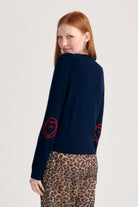 Red haired female model wearing Jumper1234 Navy cashmere crew neck jumper with red love heart intarsia elbow patches facing away from the camera