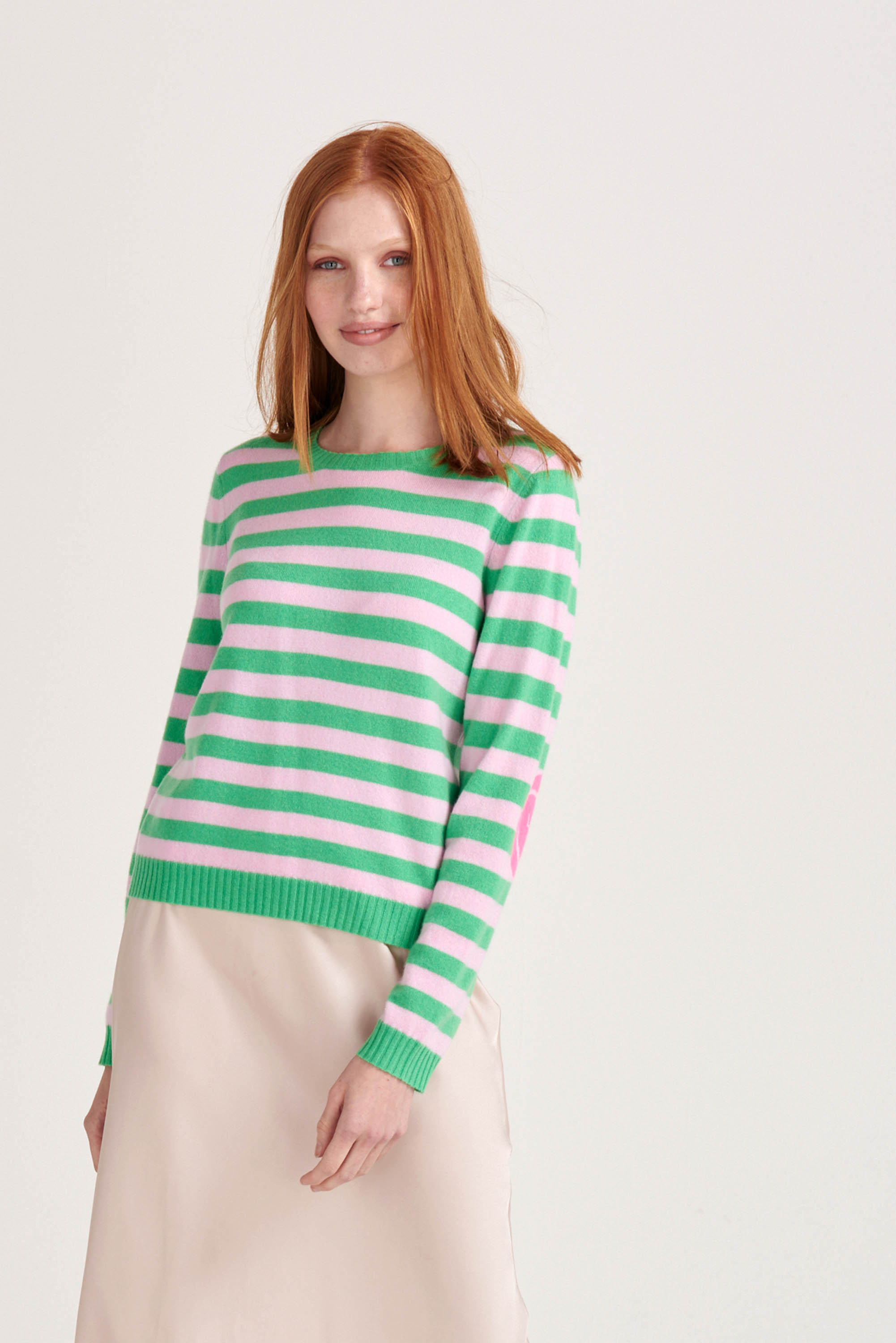 Red haired female model wearing Jumper1234 Bright green and pink stripe cashmere crew neck jumper with neon pink love heart intarsia elbow patches