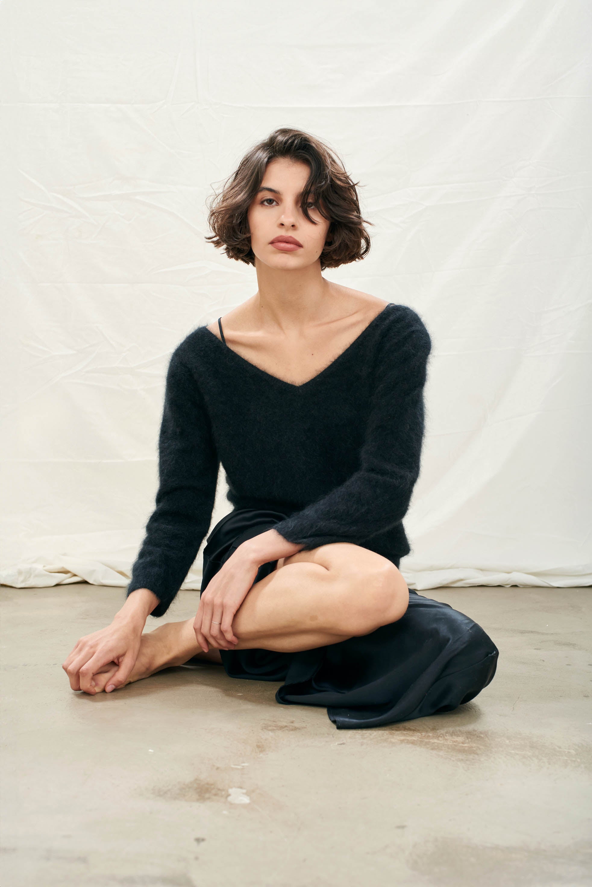 Female model wearing Jumper1234 black brushed cashmere crew with front and back vee and 3/4 length sleeves  sat on the floor