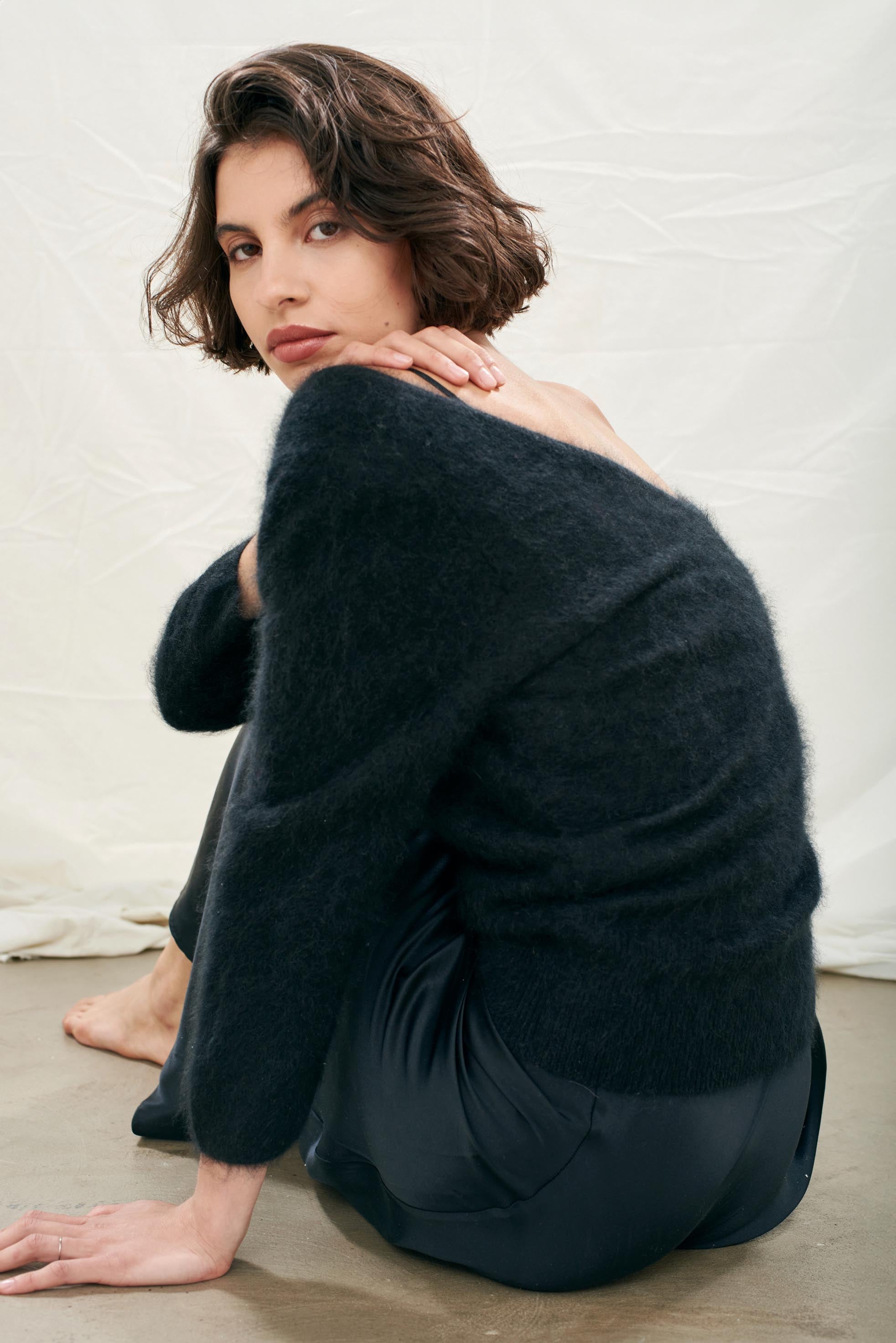 Female model wearing Jumper1234 black brushed cashmere crew with front and back vee and 3/4 length sleeves sat on the floor facing away from the camera