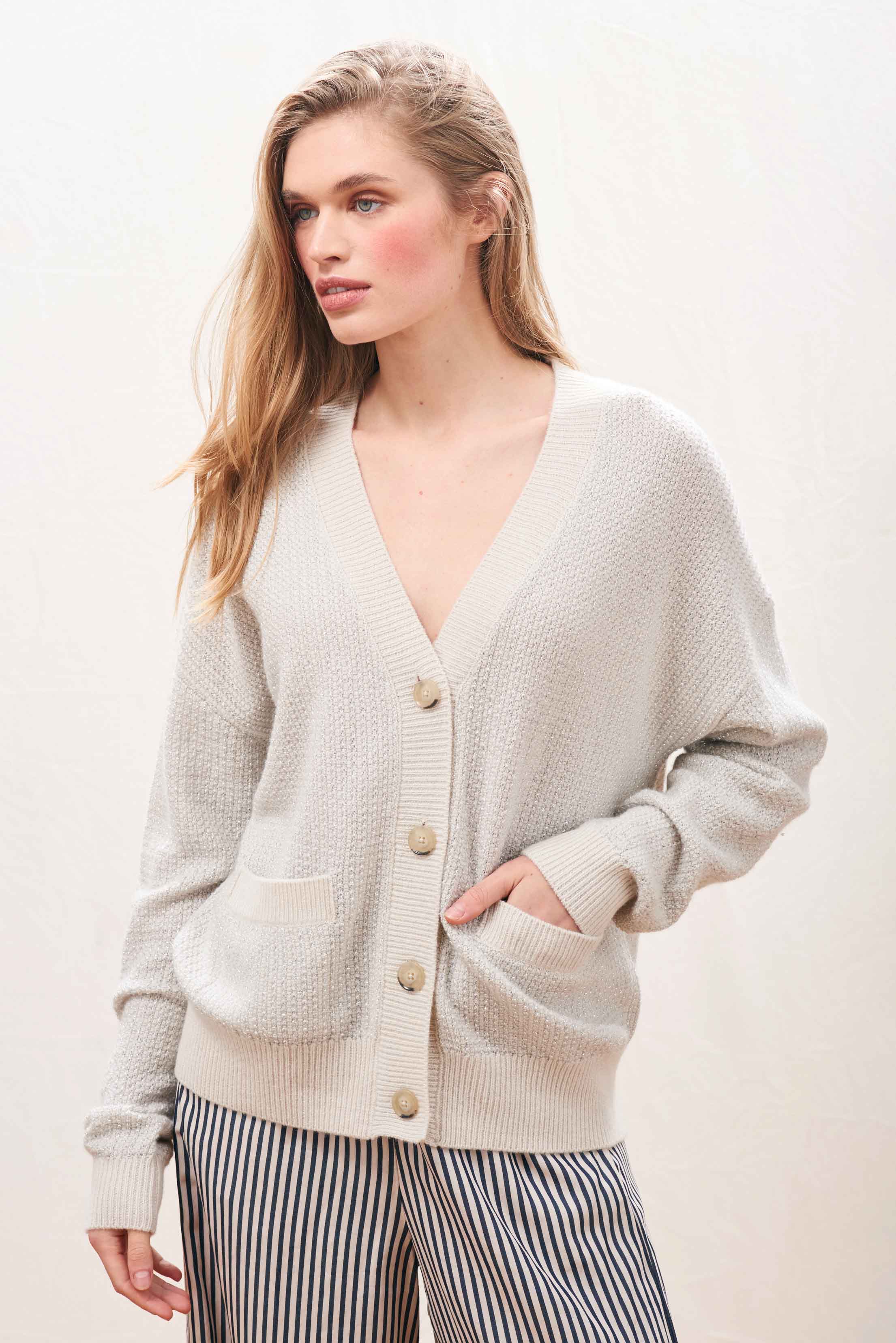Female model wearing Jumper 1234 Oversize cashmere and wool cardigan in stone with silver lurex running through the birdseye texture.