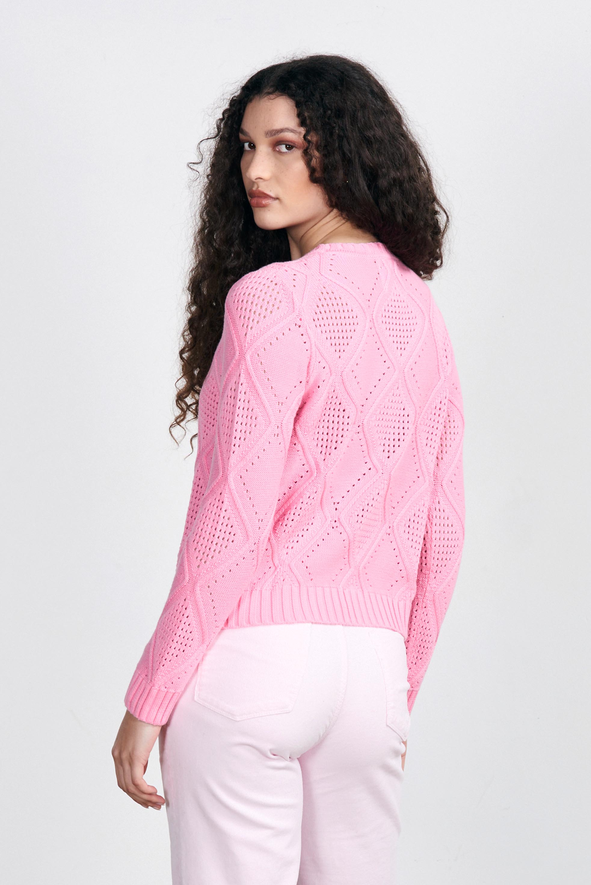 Brown haired female model wearing Jumper1234 Pink cotton crew neck jumper with a diamond texture stitch pattern facing away from the camera
