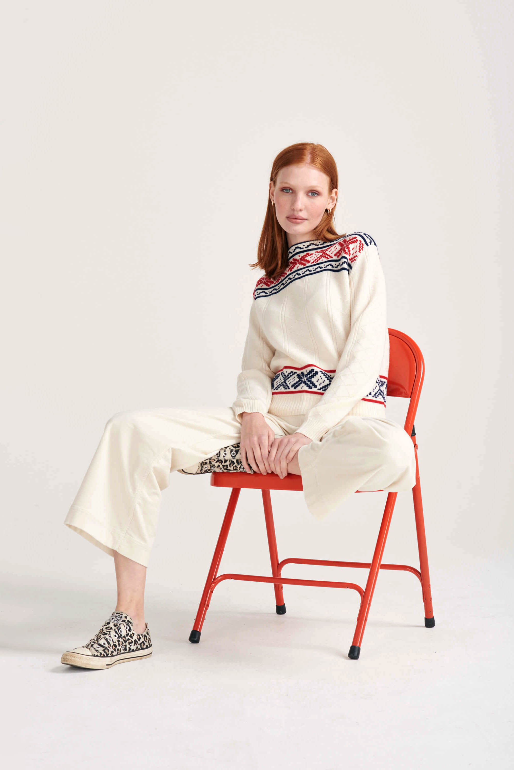 Ginger female model sat wearing Jumper1234 cream cashmere "greek guernsey" with navy and red hem and yolk detail