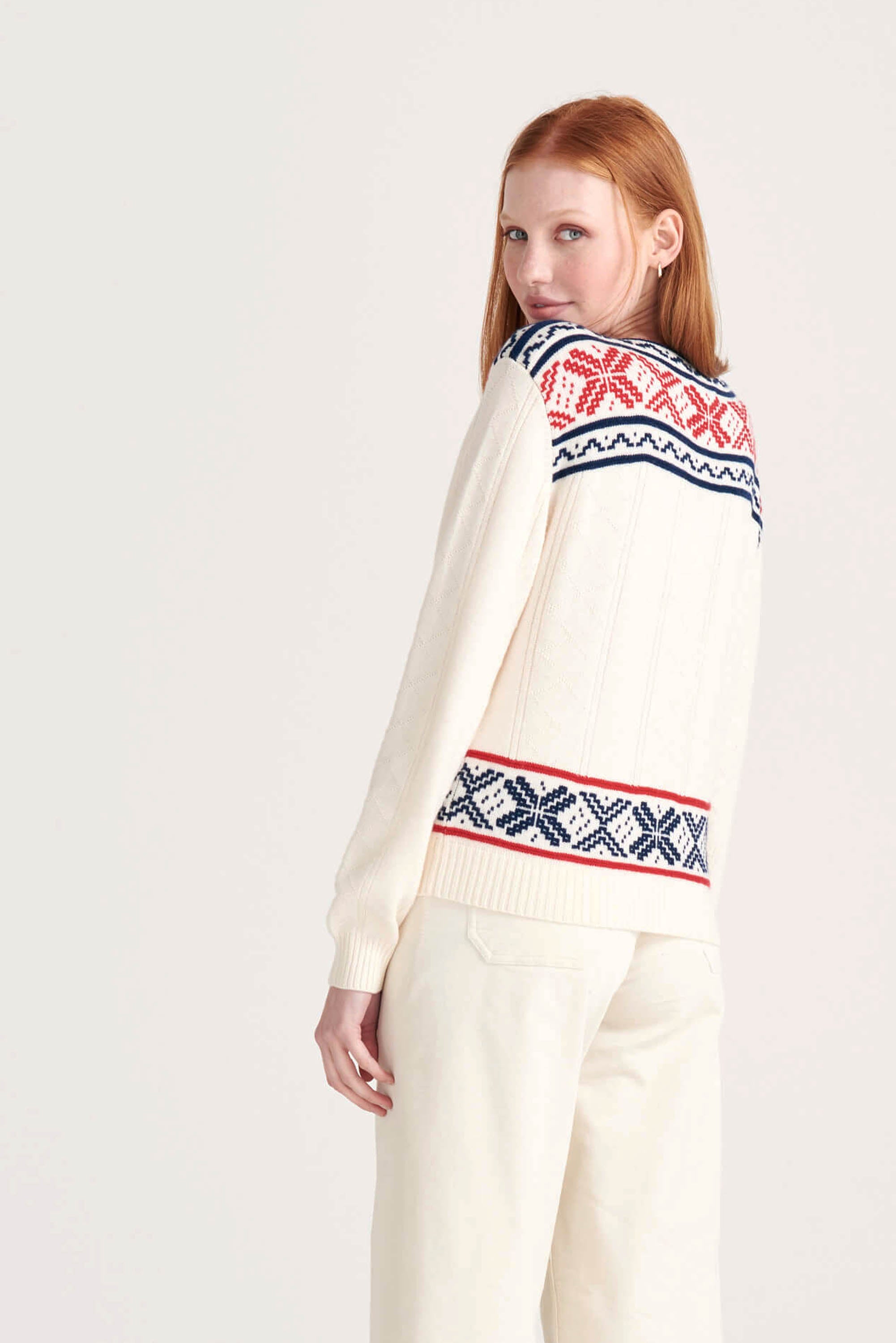 Ginger female model wearing Jumper1234 cream cashmere "greek guernsey" with navy and red hem and yolk detail facing away from the camera