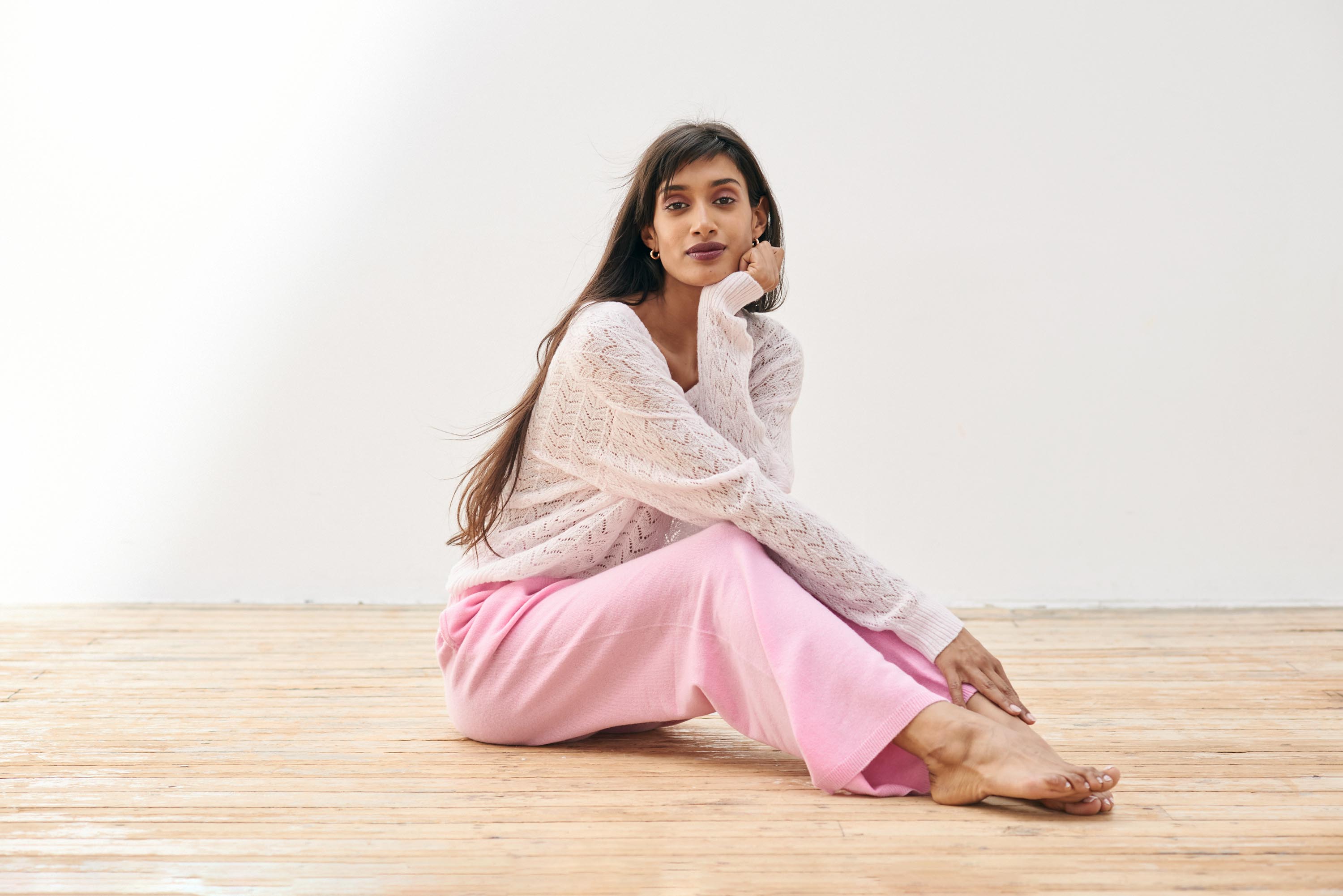Brown haired female model wearing Jumper1234 pale pink lightweight merino "Lace Vee" sat on the floor