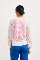 Brown haired female model wearing Jumper1234 pale pink lightweight merino "Lace cardigan" facing away from the camera