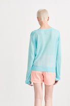 Blonde female model wearing Jumper1234 turquoise lightweight merino "Balloon Sleeve crew" facing away from the camera