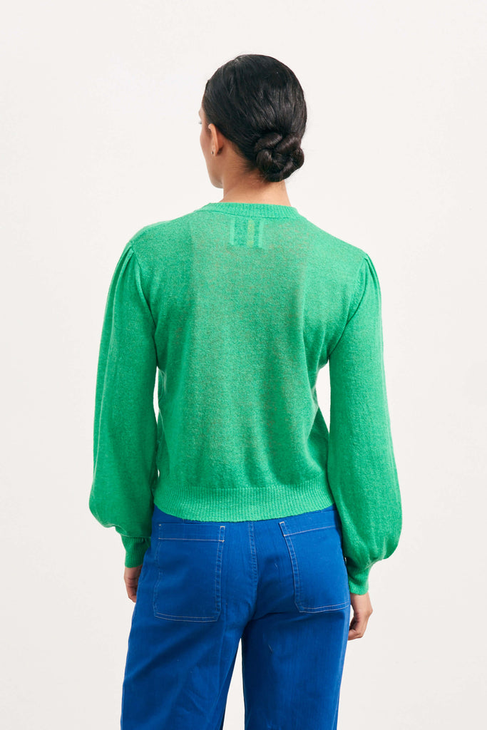 Brown haired female model wearing Jumper1234 bright green lightweight merino "Puff Sleeve cardigan" facing away from the camera