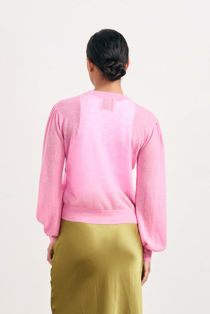 Brown haired female model wearing Jumper1234 pink lightweight merino "Puff Sleeve cardigan" facing away from the camera