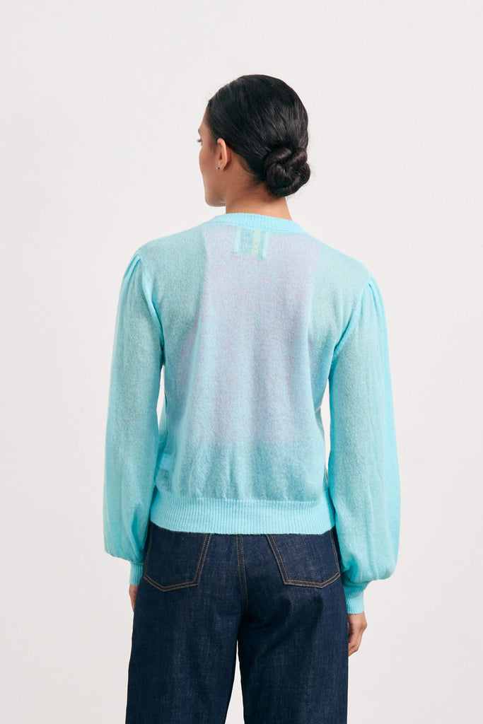 Brown haired female model wearing Jumper1234 turquoise lightweight merino "Puff Sleeve cardigan" facing away from the camera