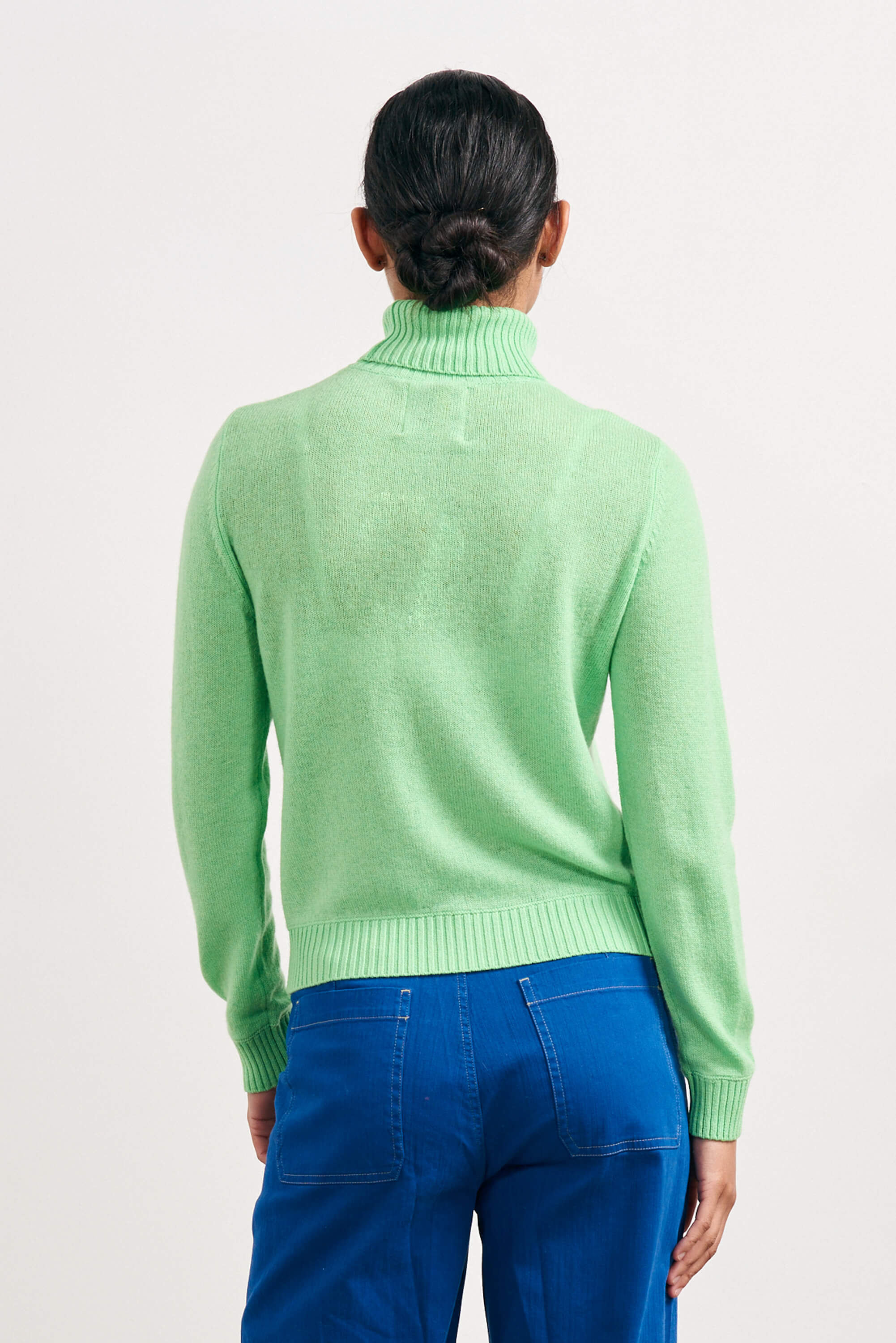 Brown haired female model wearing Jumper1234 lightweight cashmere roll neck in apple green facing away from the camera