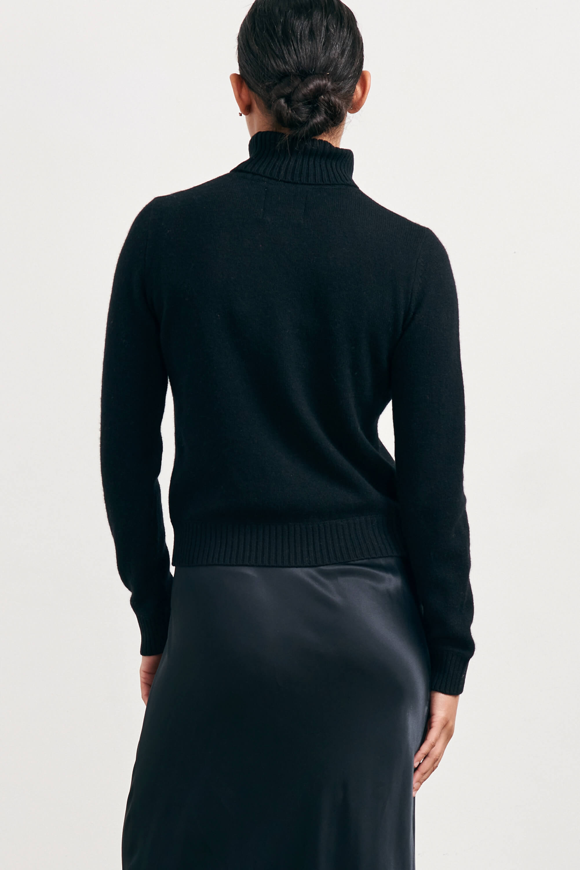 Brown haired female model wearing Jumper1234 lightweight cashmere roll neck in black facing away from the camera