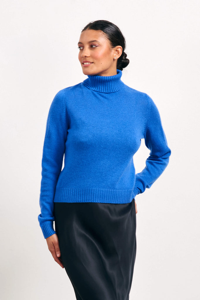 Brown haired female model wearing Jumper1234 lightweight cashmere roll neck in bright blue 