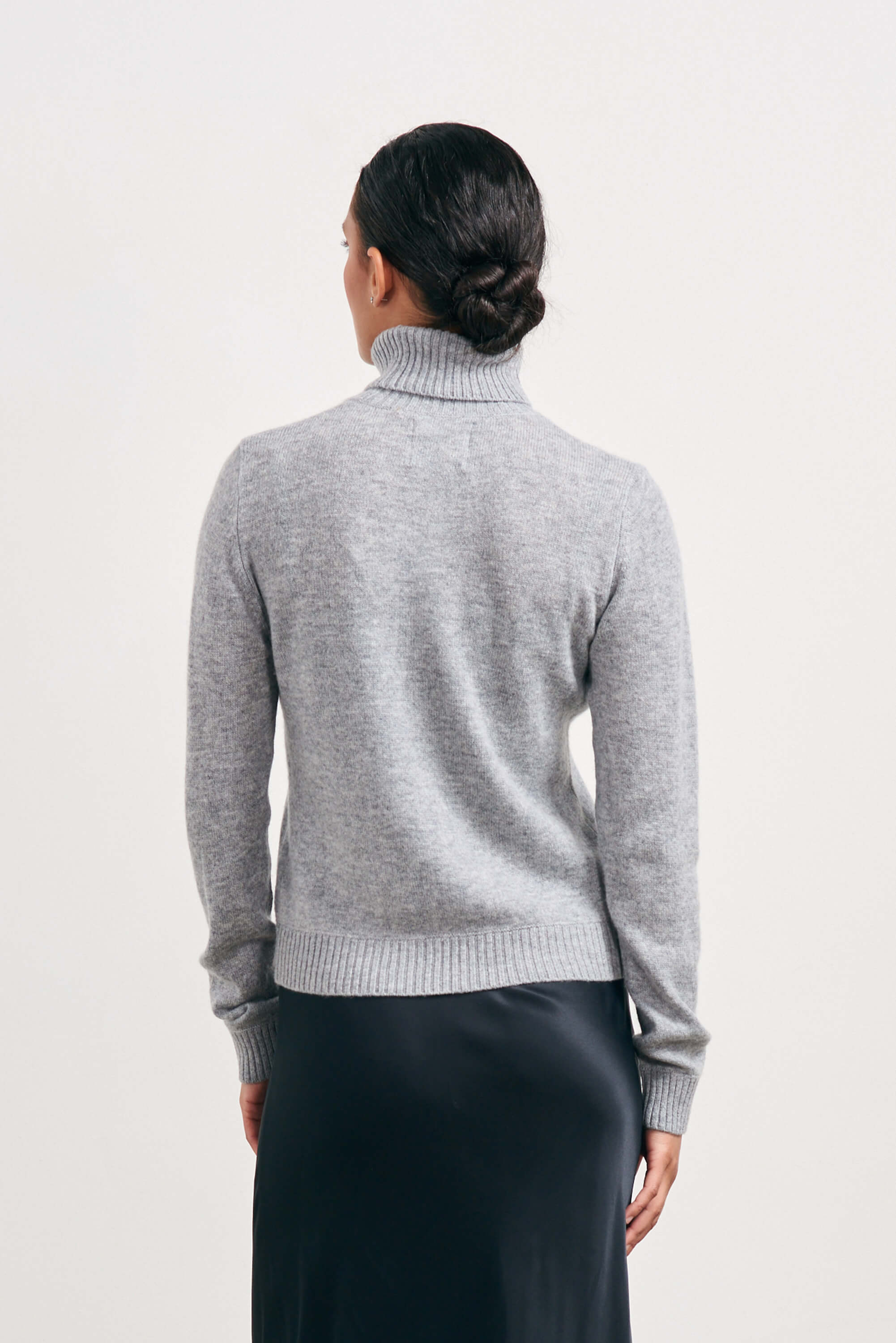 Brown haired female model wearing Jumper1234 lightweight cashmere roll neck in mid grey facing away from the camera