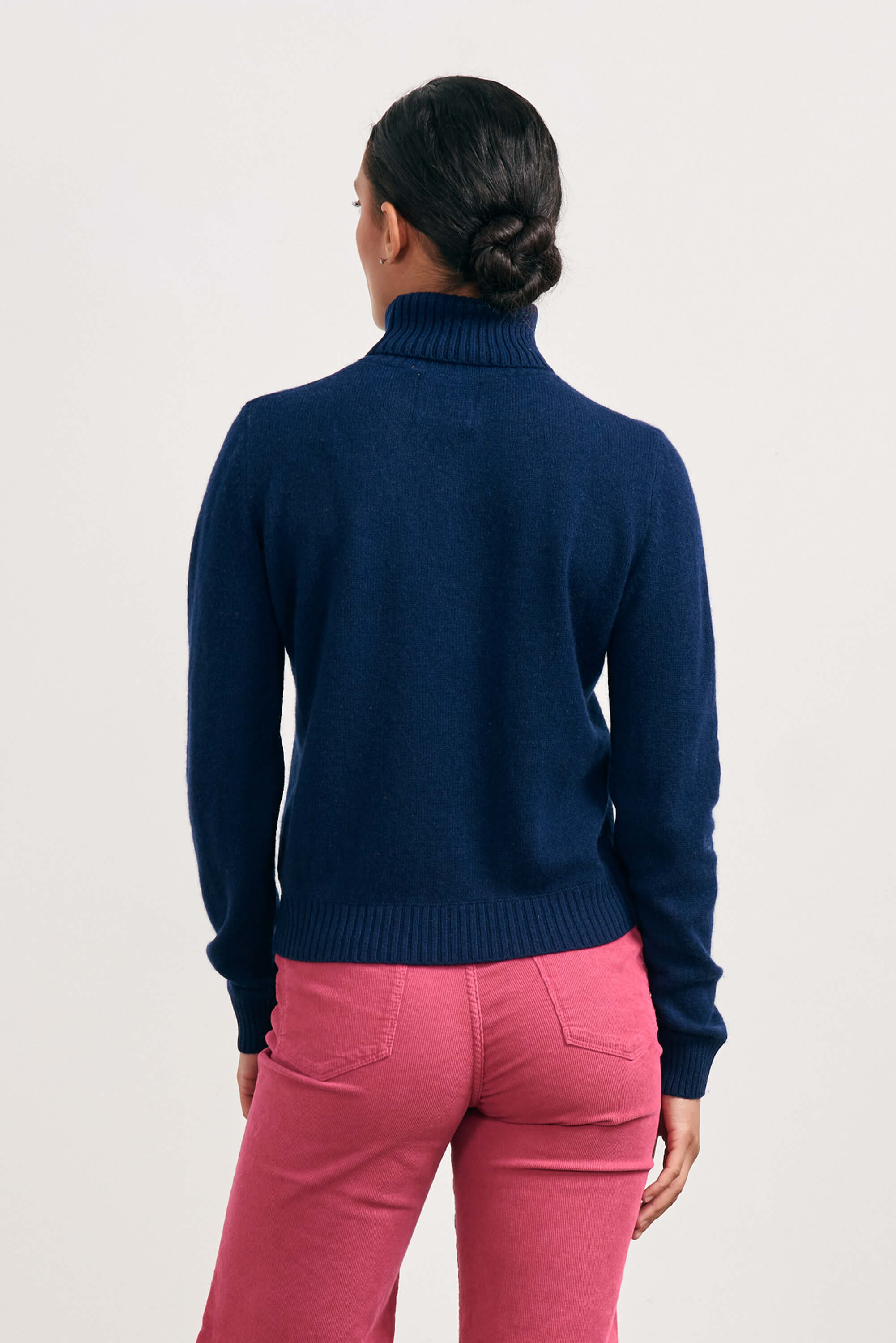 Brown haired female model wearing Jumper1234 lightweight cashmere roll neck in navy facing away from the camera
