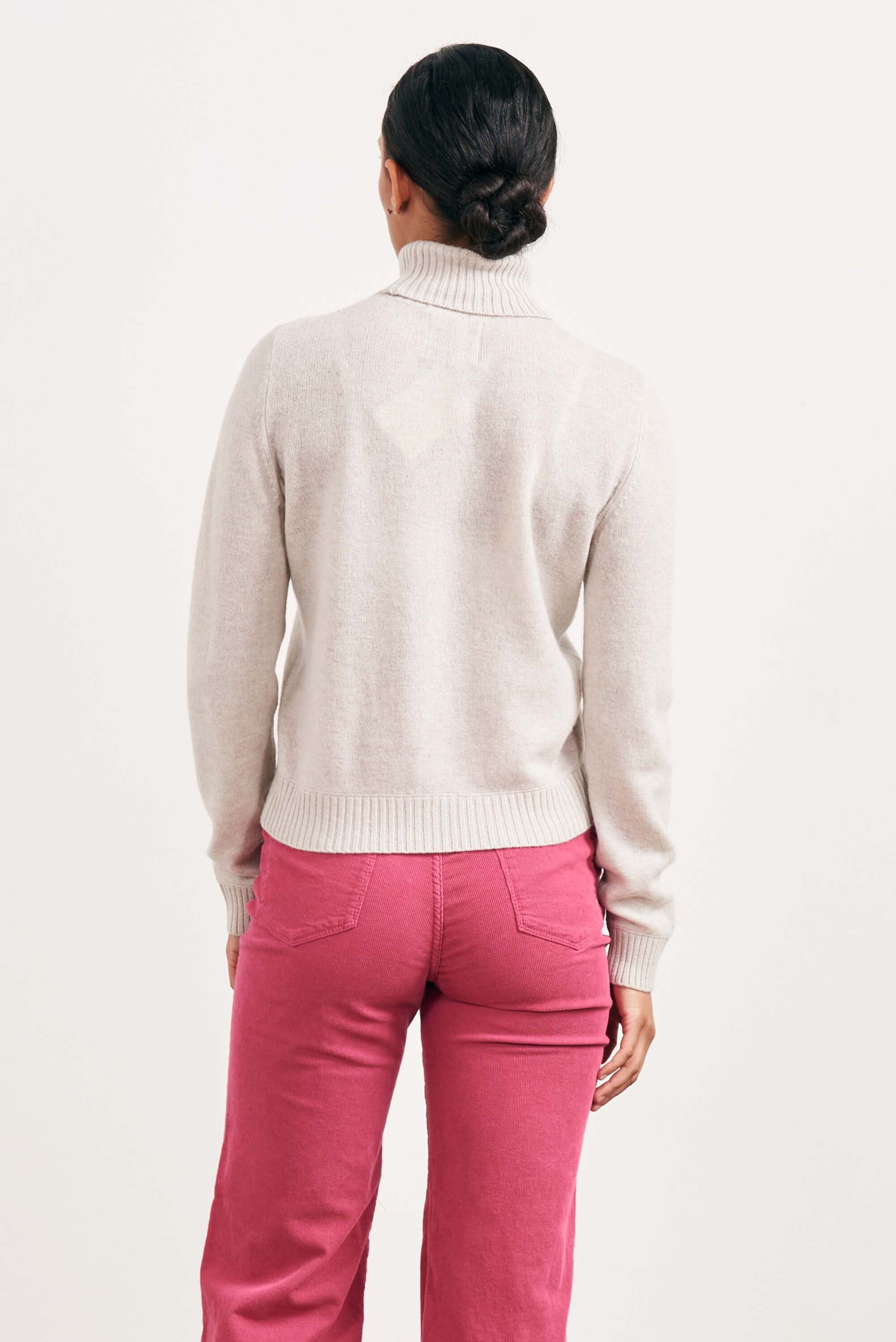 Brown haired female model wearing Jumper1234 lightweight cashmere roll neck in cream facing away from the camera