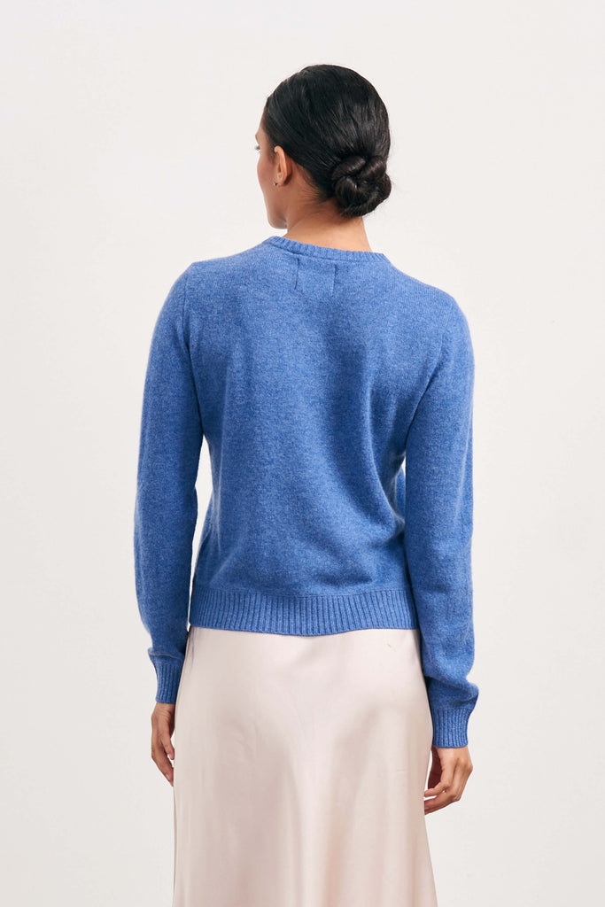 Brown haired female model wearing Jumper1234 lightweight cashmere crew neck in blue facing away from the camera