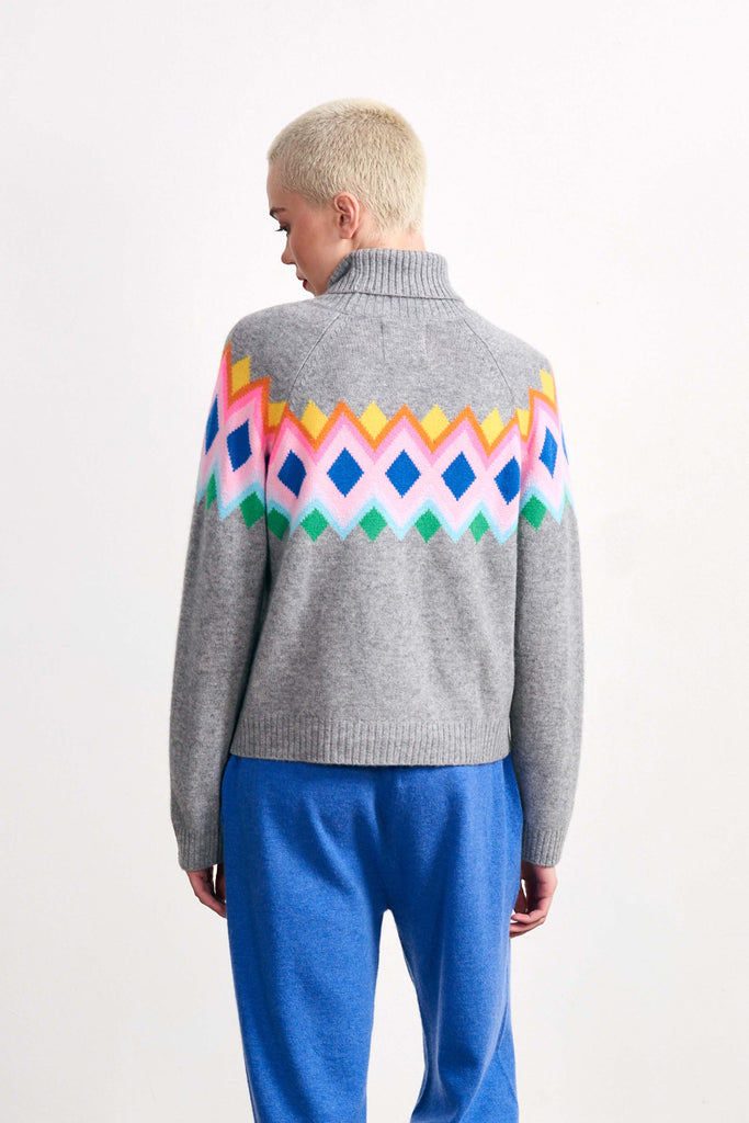 Blonde female model wearing Jumper 1234 mid grey heavier weight cashmere roll neck, with an intarsia Fairisle panel back and front in a fabulous combination of bright colours facing away from the camera