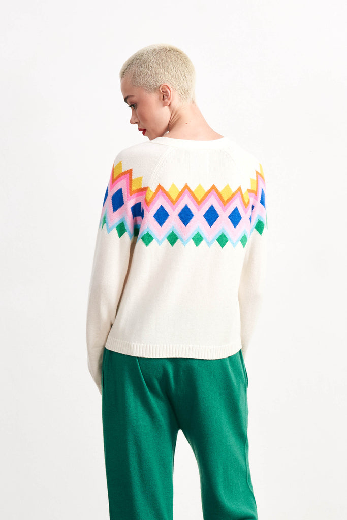 Blonde female model wearing Jumper 1234 cream heavier weight cashmere vee neck, raglan sleeve cardigan with an intarsia Fairisle panel back and front in a fabulous combination of bright colours. facing away from the camera