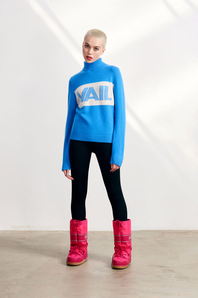 Blonde female model wearing Jumper 1234 sky blue heavier weight roll neck cashmere and wool jumper with a cream panel and 'Vail' intarsia in sky blue