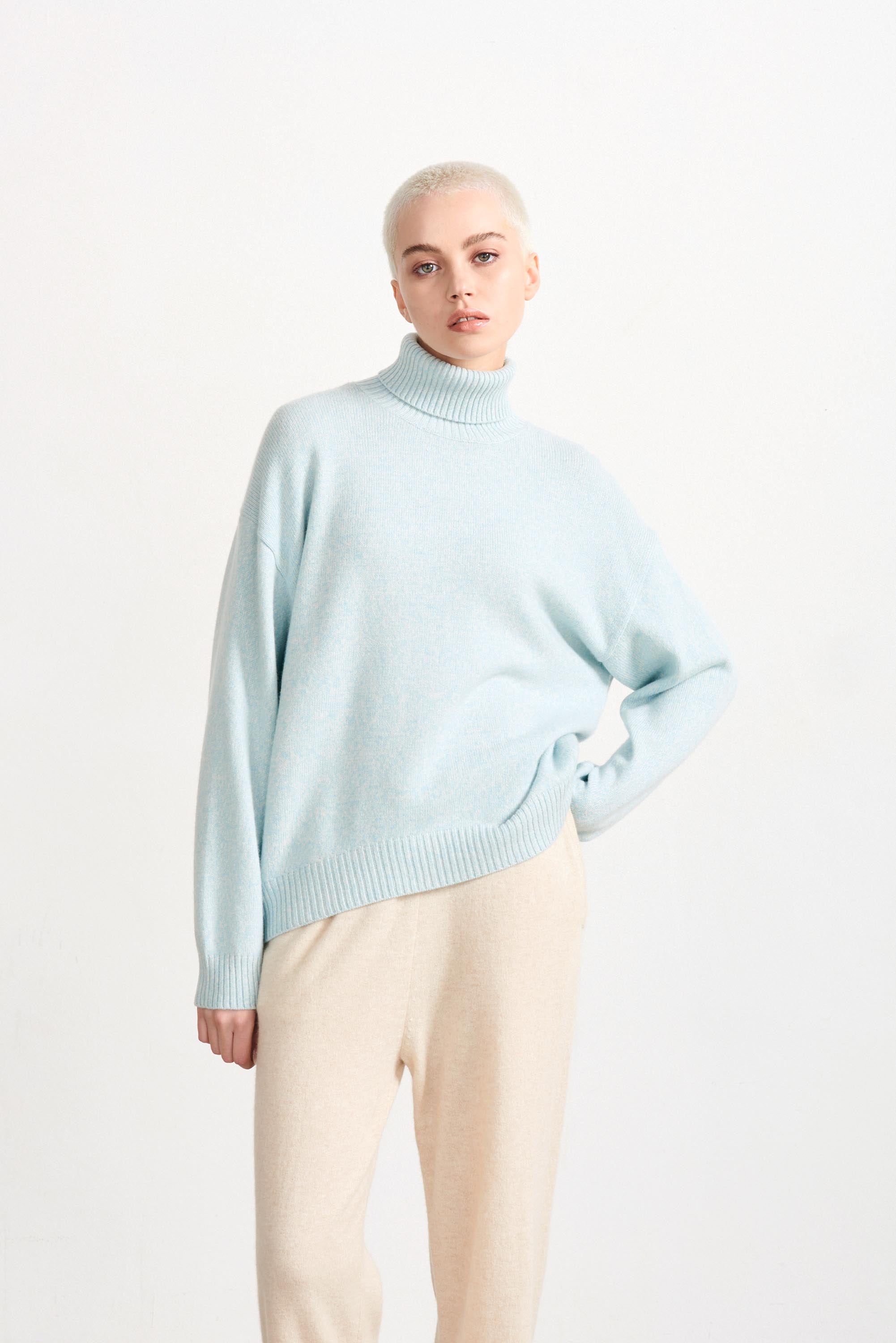 Blonde haired female model wearing Jumper 1234 cashmere and wool heavier weight oversized roll neck jumper in ice blue marl