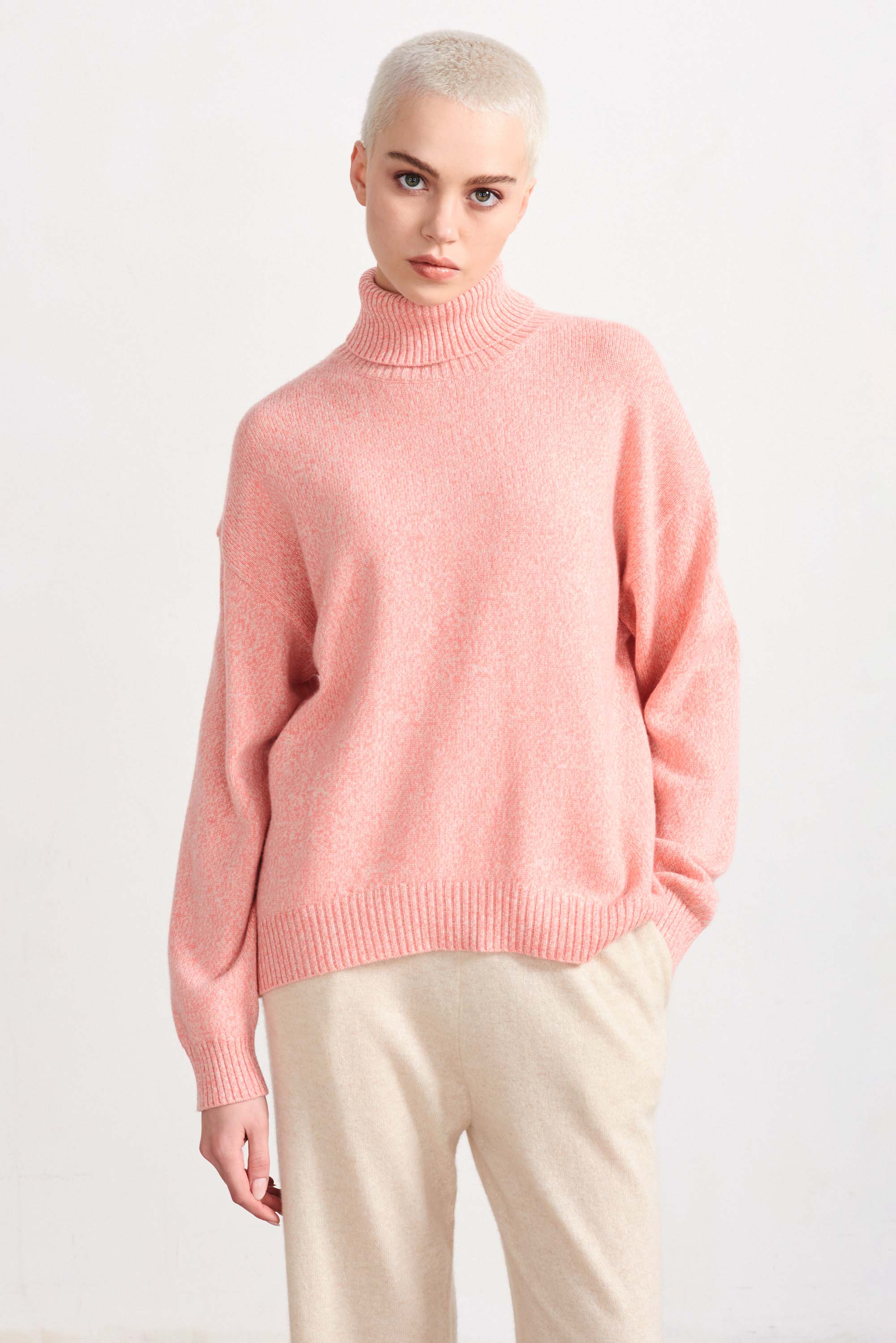 Blonde female model wearing Jumper 1234 cashmere and wool heavier weight oversized roll neck jumper in coral marl