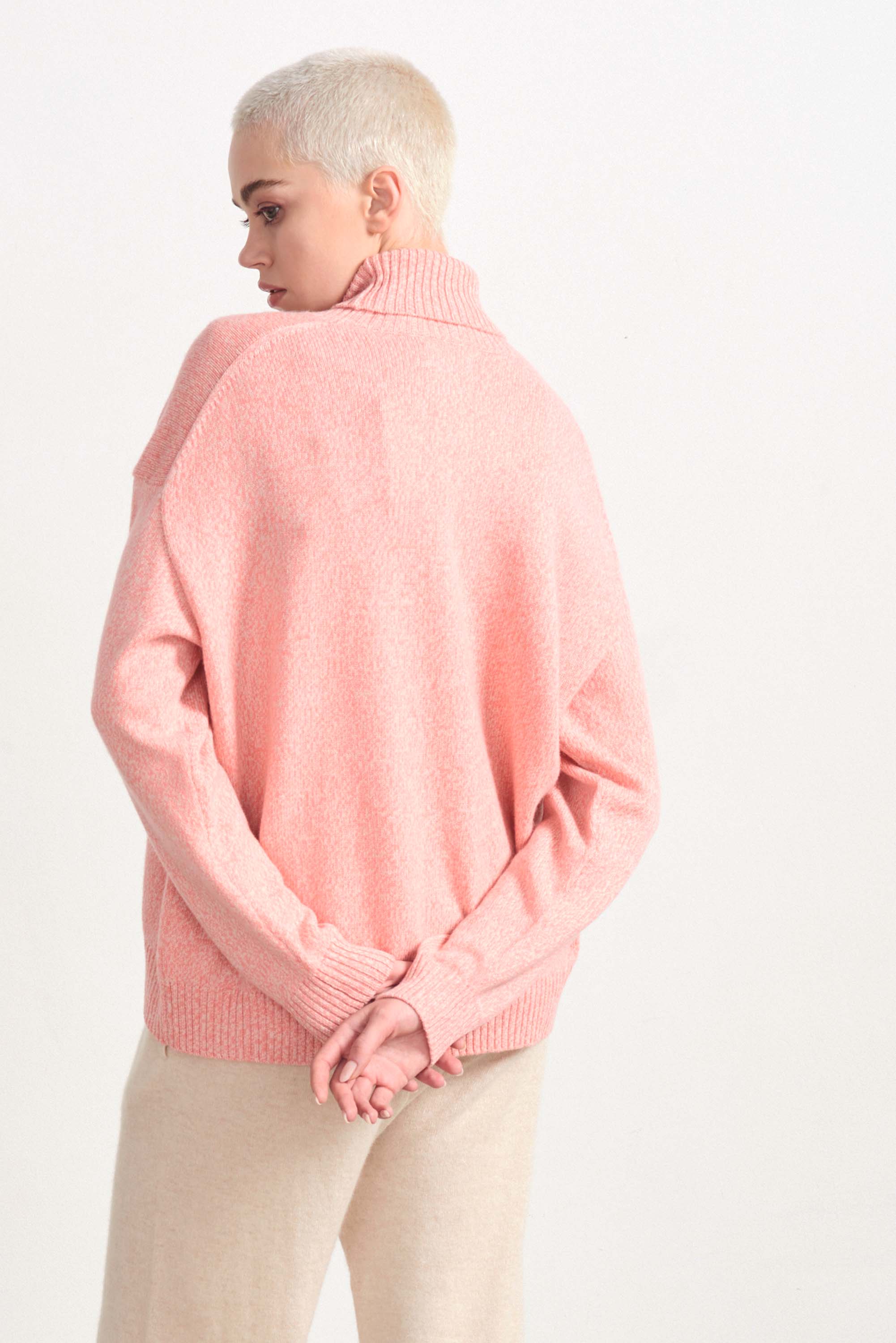 Blonde female model wearing Jumper 1234 cashmere and wool heavier weight oversized roll neck jumper in coral marl facing away from the camera