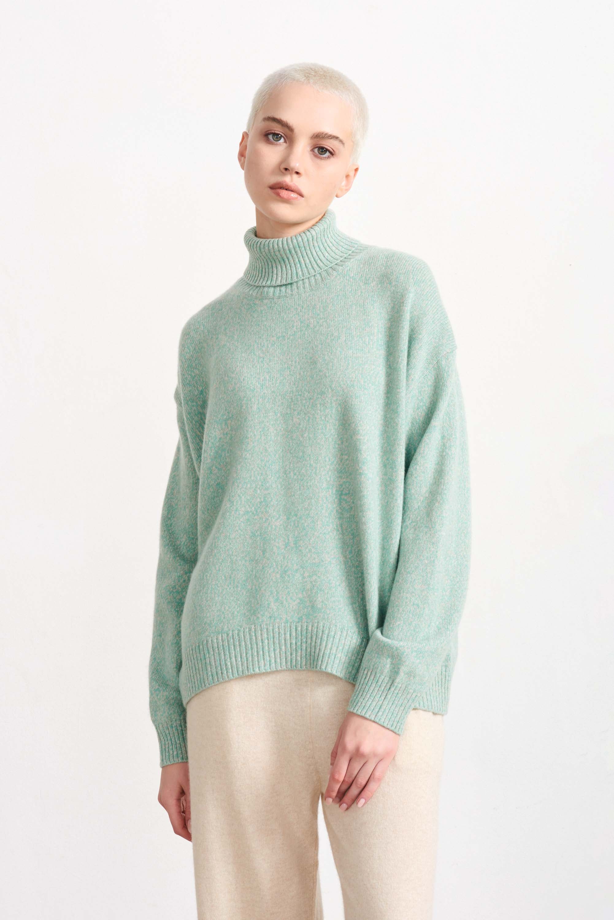 Blonde haired female model wearing Jumper 1234 cashmere and wool heavier weight oversized roll neck jumper in sage green marl