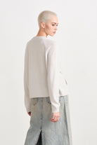 Blonde female model wearing Jumper 1234 cashmere and wool heavier weight round neck cardigan in cream marl facing away from the camera