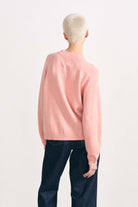 Blonde female model wearing Jumper 1234 cashmere and wool heavier weight round neck cardigan in coral marl facing away from the camera