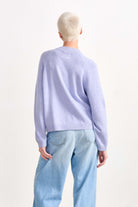 Blonde female model wearing Jumper 1234 cashmere and wool heavier weight round neck cardigan in violet marl facing away from the camera