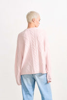 Blonde female model wearing Jumper 1234 cashmere and wool heavier weight Aran crew neck jumper in pale pink marl facing away from the camera