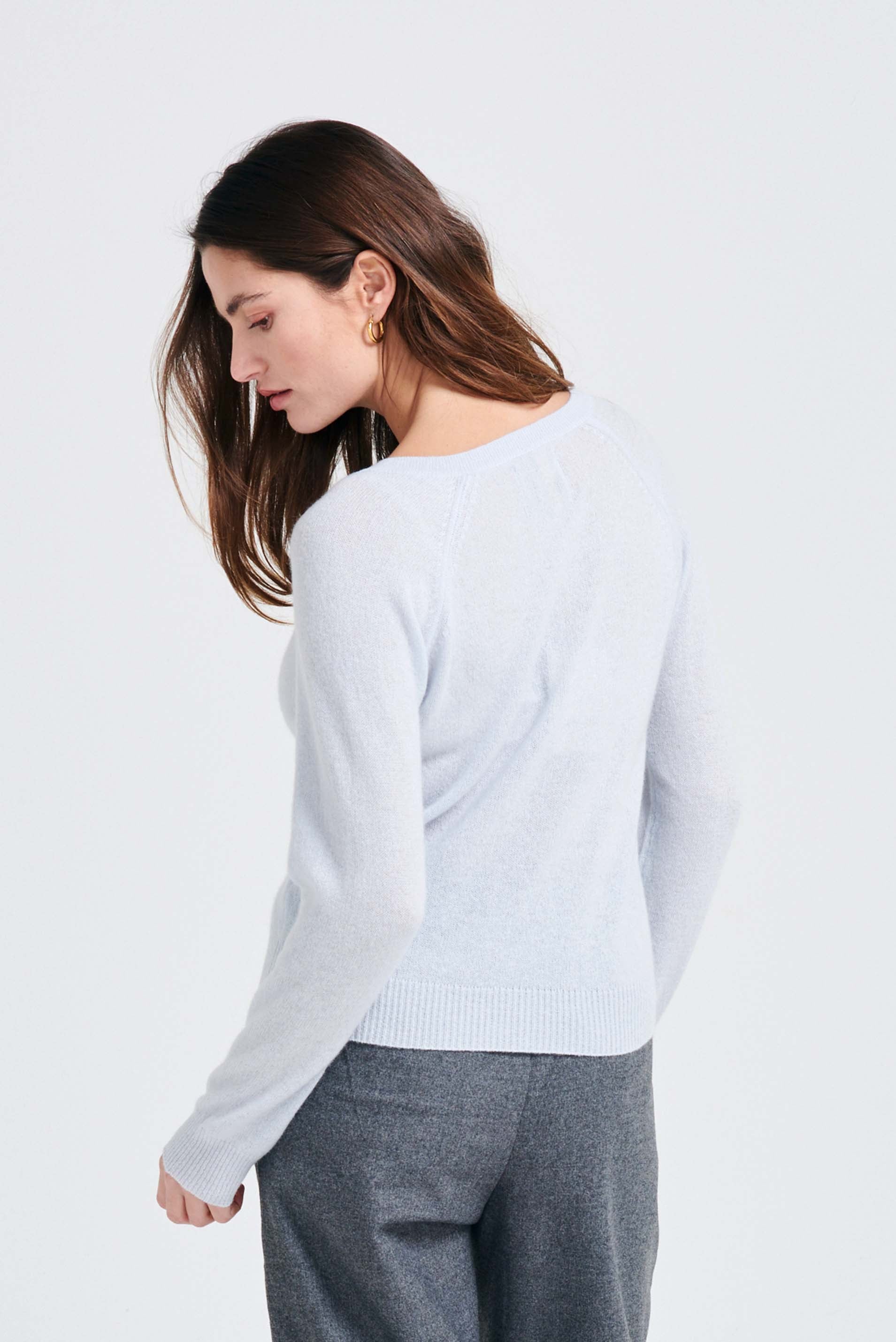 Brown haired female model wearing Jumper1234 pale blue lighter weight vee neck cashmere jumper facing away from the camera