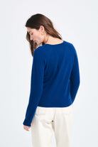 Brown haired female model wearing Jumper1234 Denim blue lighter weight vee neck cashmere jumper facing away from the camera