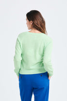 Brown haired female model wearing Jumper1234 Lime green lighter weight vee neck cashmere jumper facing away from the camera