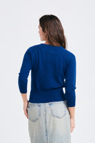 Brown haired female model wearing Jumper1234 neat fit cashmere round neck cardigan in denim blue facing away from the camera 