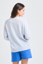 Brown haired female model wearing Jumper1234 Oversize cashmere vee neck cardigan in pale blue facing away from the camera